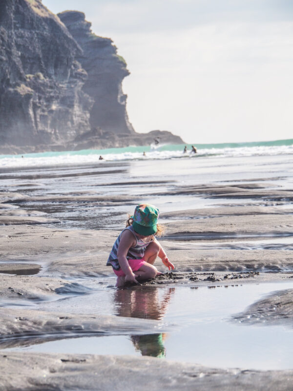 young girl playing in the tide pools at Piha beach, North Island, New Zealand with kids