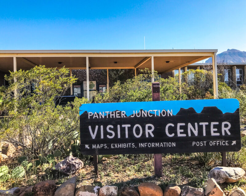 Panther Junction visitor center at Big Bend National Park, Texas; painted sign and green shrubs in foreground, low flat building and blue sky in background