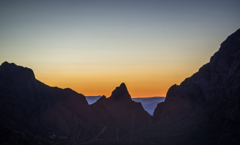 Big Bend National Park sunset through the Window - mountain peak in the middle of orange sunset with blue mountains in background