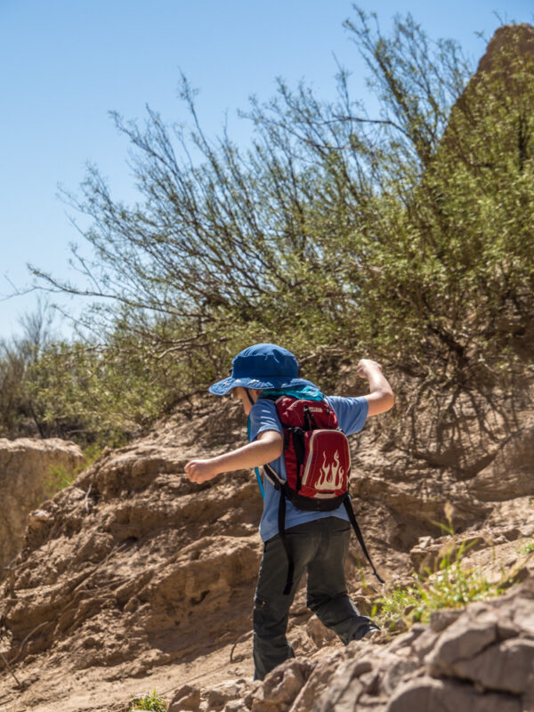 Young boy with red backpack and blue hat hiking in Big Bend National Park, Texas