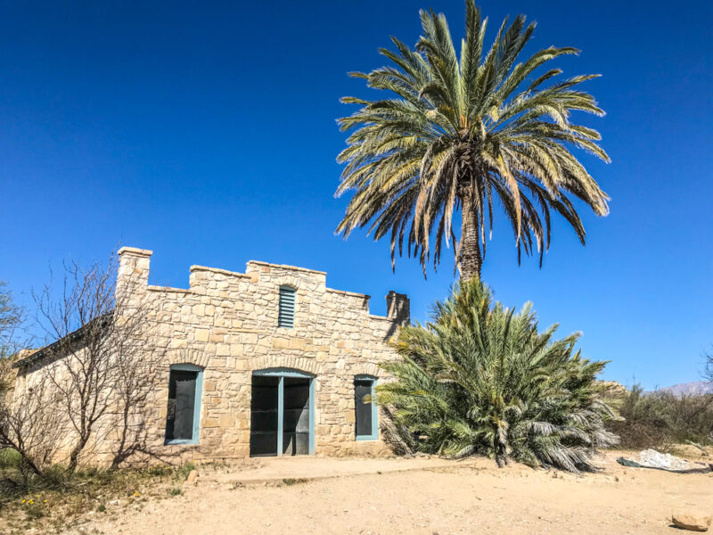 Old stone building with palm tree in front, original Big Bend hot springs hotel in Big Bend National Park, Texas