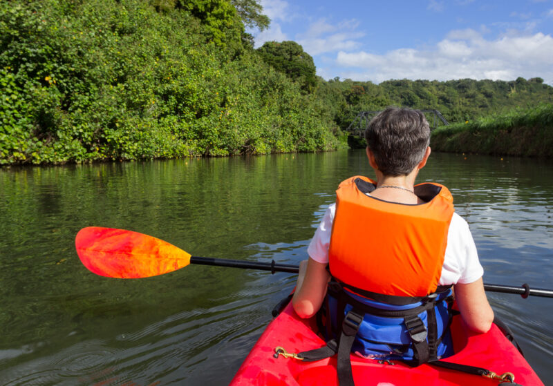 Retired caucasian lady in a red canoe or sea kayak on Hanalei river approaching the old steel bridge in Kauai