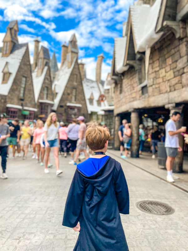 Boy in Ravenclaw robe walking through Hogsmeade at Universal Islands of Adventure with tweens