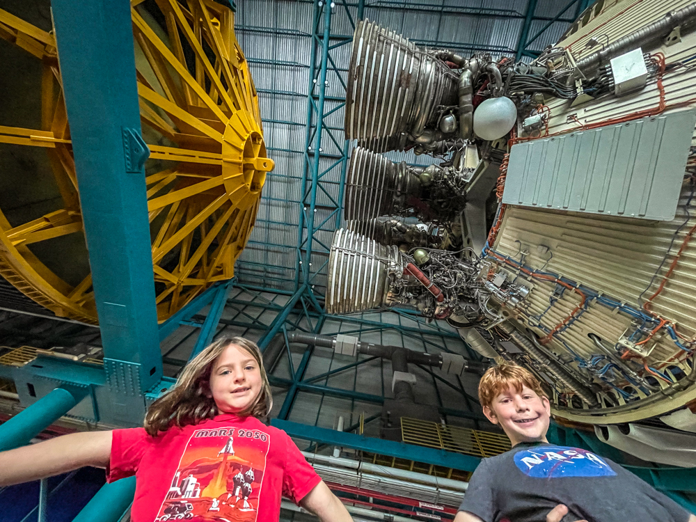 Boy and girl standing under Saturn V rocket at Kennedy Space Center with kids