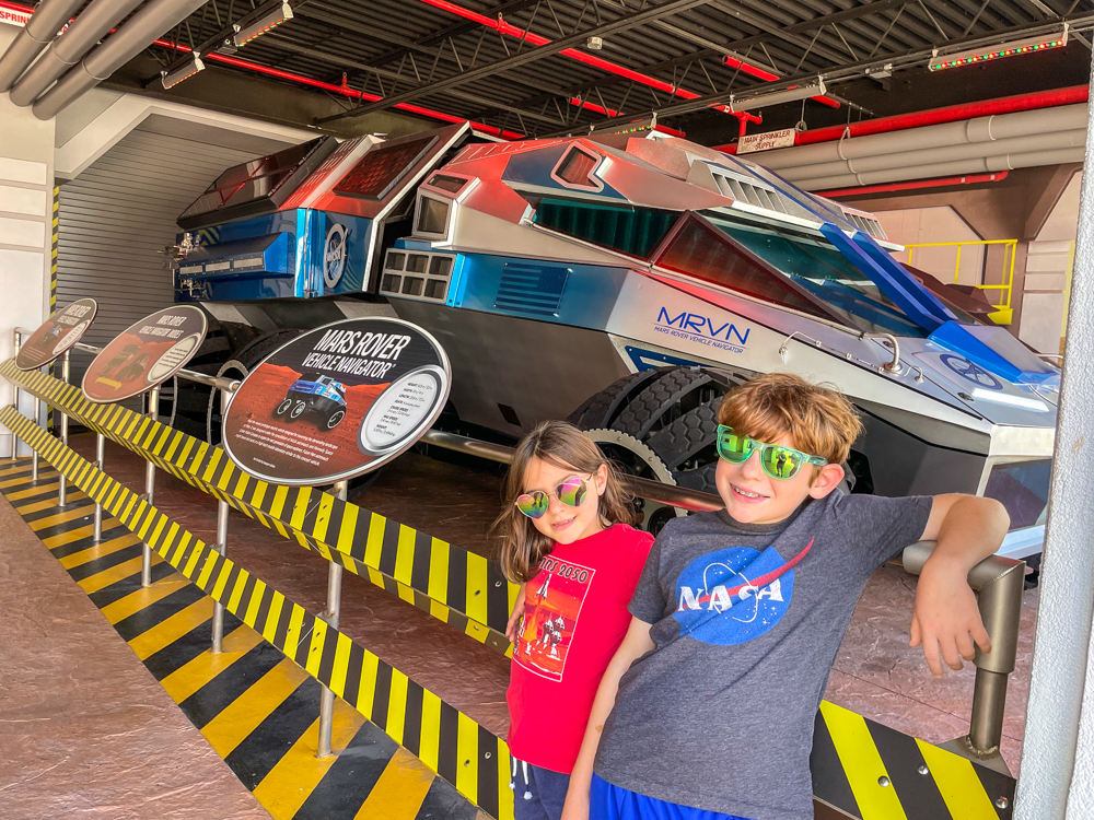 Two children wearing sunglasses in front of Mars rover MRVN at Kennedy Space Center with kids